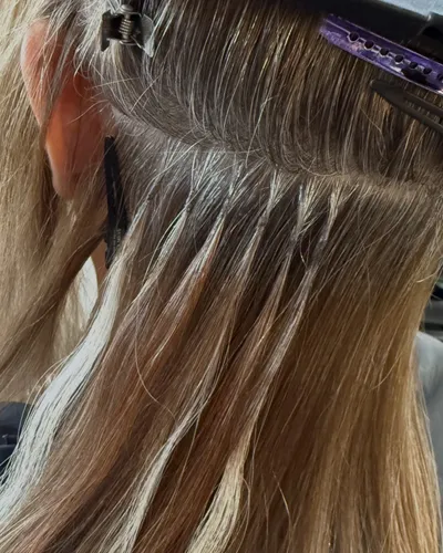 Close-up of keratin fusion extension bonds being installed in bronde balayage hair